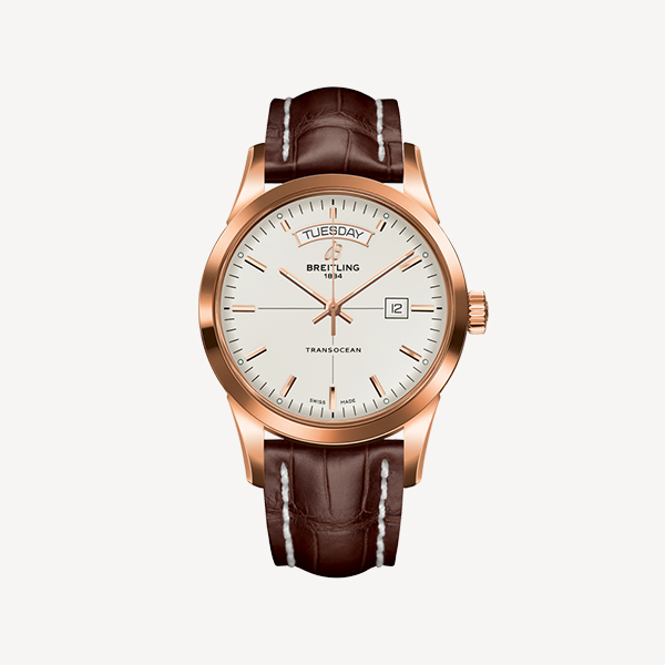 Eine Breitling Transocean-Uhr mit Roségoldgehäuse, weißem Zifferblatt und braunem Lederarmband. Das Zifferblatt ist bei Juwelier Morawitz in Düsseldorf erhältlich und verfügt über Tages- und Datumsfenster bei 12 bzw. 3 Uhr sowie einfache Stundenmarkierungen und ein Logo unter dem Tagesfenster.