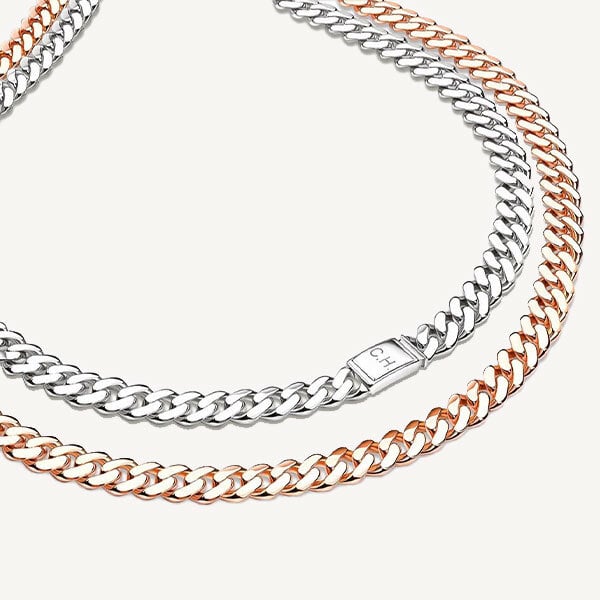 Zwei Kettenhalsketten von Juwelier Morawitz sind auf einem hellen Hintergrund ineinander verschlungen. Eine Kette ist aus Silber, die andere aus Roségold. Beide haben ein stilvolles und poliertes Erscheinungsbild, wobei ein einzelner Verschluss an der Silberkette mit den eingravierten Initialen „C H“ an die zeitlose Eleganz Düsseldorfs erinnert.