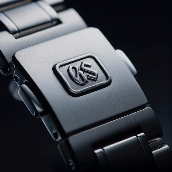 Juwelier-Morawitz-Box-Grand-Seiko-Ansicht Nahaufnahme einer Uhrschließe aus Metall mit den eingeprägten Initialen „GS“ und gebürstetem Edelstahl-Finish. Der Fokus liegt auf der detaillierten Verarbeitung und Textur des Materials, wie man sie in den exklusiven Kollektionen bei Juwelier Morawitz in Düsseldorf sieht.