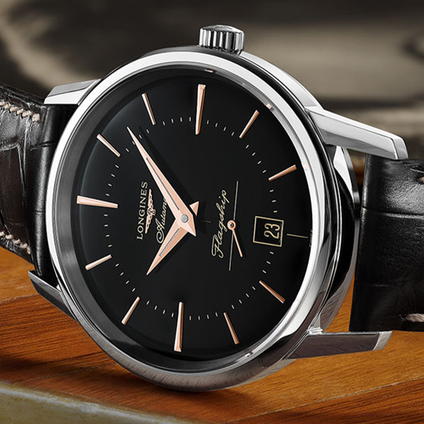 Nahaufnahme einer Longines Armbanduhr mit schwarzem Zifferblatt, roségoldenen Zeigern und Stundenmarkierungen. Die Uhr hat ein Edelstahlgehäuse und ein schwarzes Lederarmband. Das Datumsfenster zeigt die Zahl 23. Auf dem Zifferblatt ist in Schreibschrift der Schriftzug „Flagship“ aufgedruckt, erhältlich bei Juwelier Morawitz in Düsseldorf.