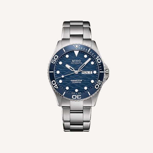 Eine silberne Mido Ocean Star-Uhr von Juwelier Morawitz in Düsseldorf verfügt über ein poliertes Metallarmband, ein blau strukturiertes Zifferblatt, weiße Stundenmarkierungen und leuchtende Zeiger. Die blaue Lünette mit weißen Ziffern rundet den Look ab und die Uhr zeigt Tag und Datum auf der 3-Uhr-Position an.