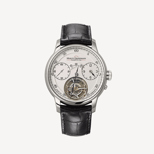 Eine Luxusarmbanduhr von Juwelier Morawitz mit silbernem Gehäuse, weißem Zifferblatt und schwarzem Lederarmband. Das Zifferblatt verfügt über schwarze Ziffern, drei Hilfszifferblätter und ein freiliegendes Stück komplizierten mechanischen Uhrwerks auf der 6-Uhr-Position. Der Markenname ist auf dieser exquisiten Düsseldorfer Uhr stolz sichtbar.