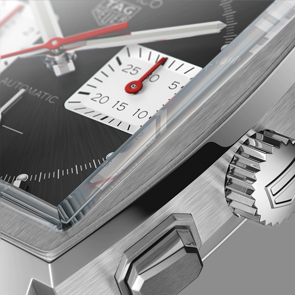 Nahaufnahme einer Luxusarmbanduhr von Juwelier Morawitz, Düsseldorf, mit poliertem Edelstahlgehäuse, strukturiertem schwarzem Zifferblatt und einer Teilansicht eines Chronographen-Hilfszifferblatts mit roten und weißen Akzenten. Die Krone und der Drücker sind ebenfalls sichtbar und zeigen feine Details.