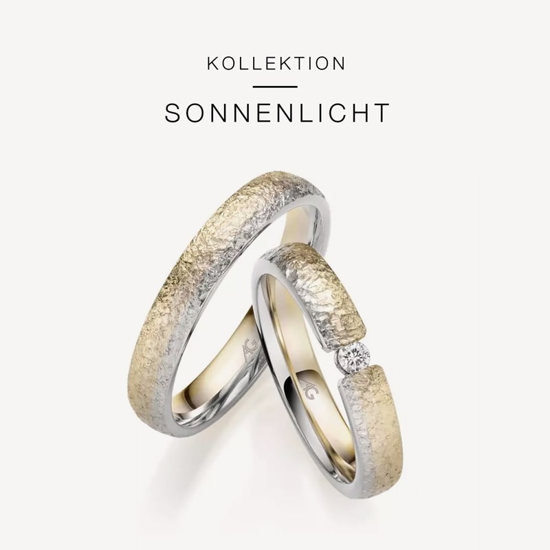 Juwelier-Morawitz-Gerstner-Kollektion-Sonnenlicht Auf weißem Untergrund sind zwei Ringe mit Struktur aus der „Kollektion Sonnenlicht“ von Juwelier Morawitz aus Düsseldorf zu sehen. Der größere Ring ist schlicht und hat eine gehämmerte Oberfläche, während der kleinere Ring eine ähnliche Struktur aufweist und mit einem kleinen, funkelnden Diamanten verziert ist.