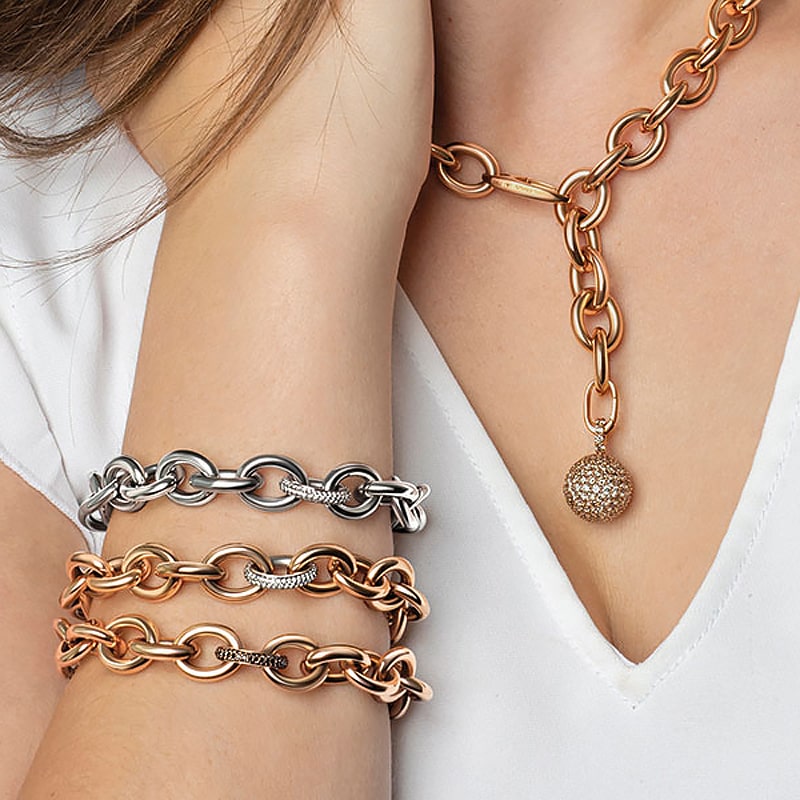 Juwelier-Morawitz-Schmuck-Emil-Kraus-Ansicht-1 Nahaufnahme einer Person mit Schmuck: eine zweifarbige Gliederkette mit rundem Anhänger von Juwelier Morawitz aus Düsseldorf und drei passende Gliederarmbänder in Gold- und Silbertönen. Die Person trägt ein weißes Top mit V-Ausschnitt.