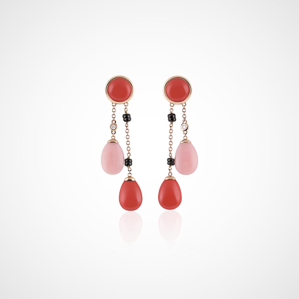 Juwelier-Morawitz-Schmucklexikon-double Ein Paar Ohrhänger von Juwelier Morawitz in Düsseldorf besteht aus runden roten Ohrsteckern, die an zwei Ketten befestigt sind. Jede Kette hat einen tropfenförmigen Anhänger, einen rosa und einen roten, mit kleinen schwarzen Perlen zwischen den Kettensegmenten. Der Hintergrund ist schlicht weiß.