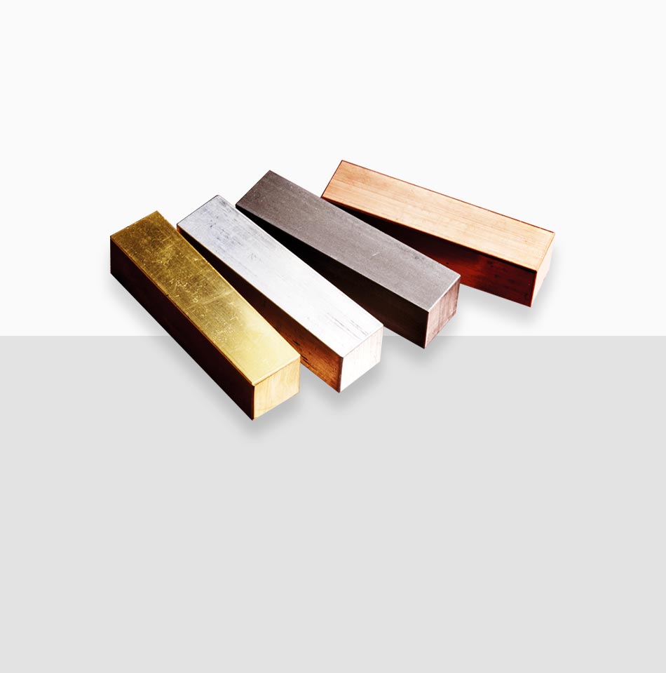 Juwelier-Morawitz-Schmucklexikon-edelmetalle Vier metallische rechteckige Stäbe, diagonal von links nach rechts auf einem weißen und grauen Hintergrund angeordnet, zeigen eine beeindruckende Palette an Materialien: Gold, Silber, Dunkelgrau und Bronze. Diese exquisite Präsentation von Edelmetallen erinnert an die feine Handwerkskunst von Juwelier Morawitz in Düsseldorf.