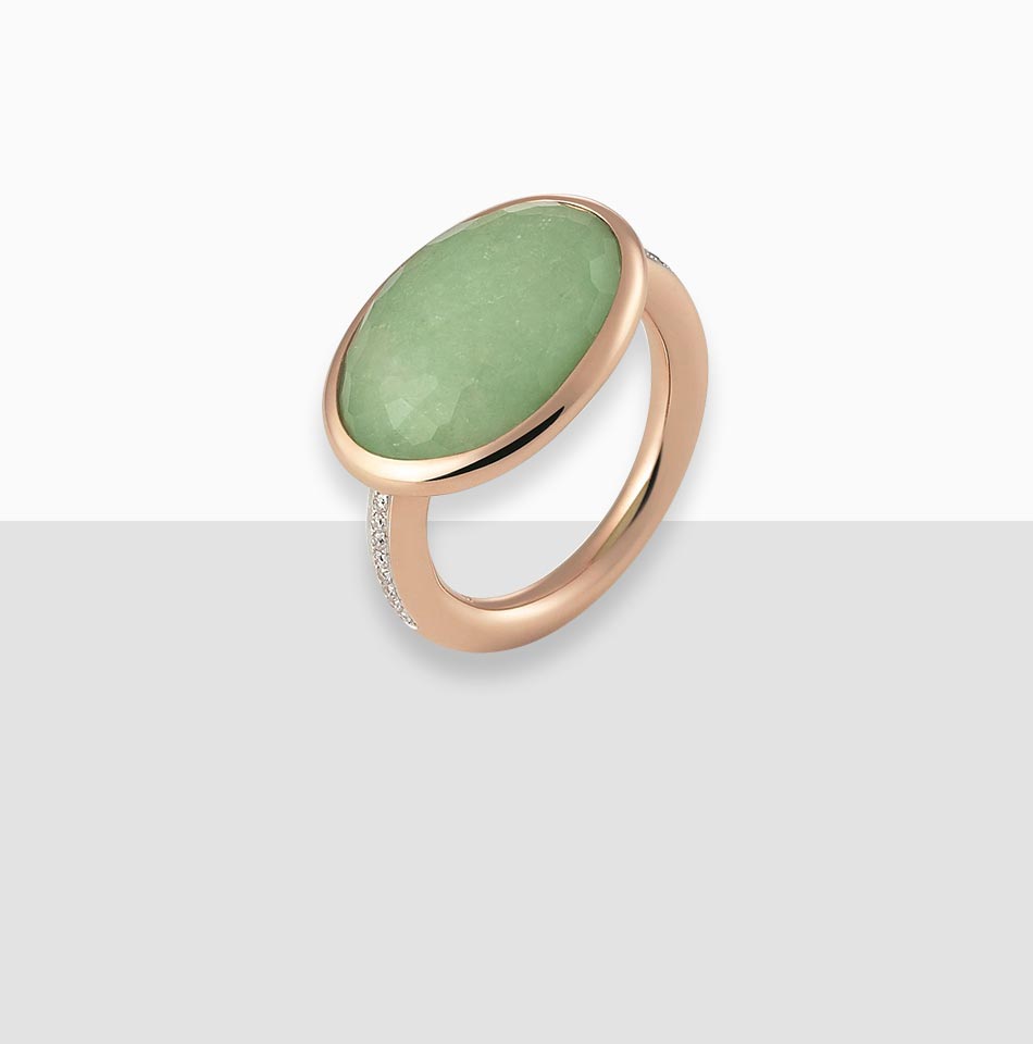 Juwelier-Morawitz-Schmucklexikon-zargenfassung Ein eleganter Ring mit einem großen ovalen grünen Edelstein in einem polierten Roségoldband mit kleinen Akzentdiamanten an der Seite des Bandes. Dieses atemberaubende Stück von Juwelier Morawitz in Düsseldorf wird vor einem klaren, minimalistischen Hintergrund präsentiert.
