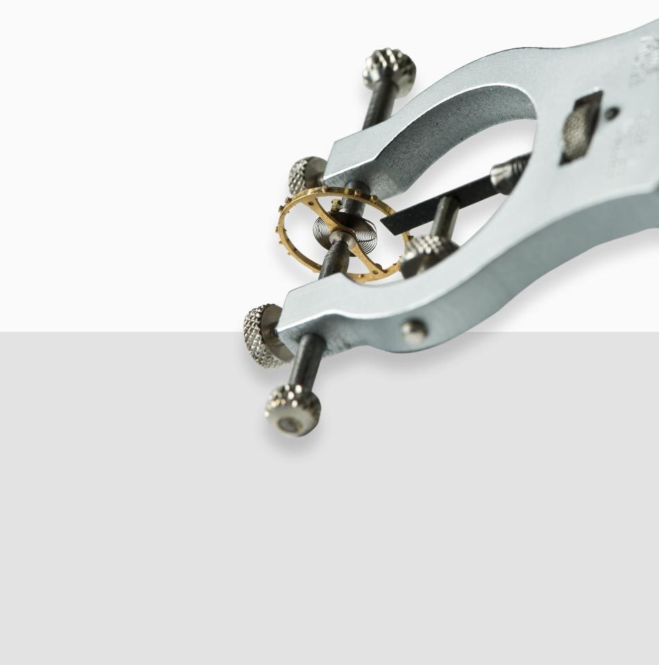 Juwelier-Morawitz-Uhrenlexikon-frequenz Eine Nahaufnahme eines speziellen Uhrmacherwerkzeugs, das ein kleines Zahnrad hält, vermutlich Teil eines Uhrwerks. Das Werkzeug, erhältlich bei Juwelier Morawitz in Düsseldorf, hat metallische Knöpfe für Feineinstellungen und ist vor einem neutralen, hellgrauen Hintergrund zu sehen.