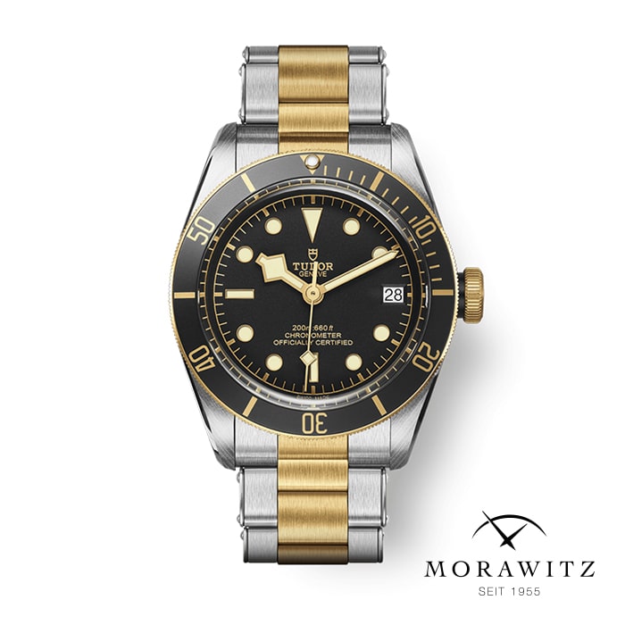 Eine Luxusarmbanduhr mit schwarzem Zifferblatt mit goldenen Akzenten, Datumsfenster und zweifarbigem Armband aus Edelstahl und Gold. Die Uhr trägt die Marke „Tudor“ und darunter das Logo „Morawitz Seit 1955“.