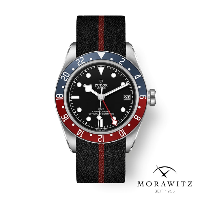 Eine Tudor-Armbanduhr mit schwarzem Zifferblatt, schwarz-rot gestreiftem Stoffarmband und blau-roter Lünette. Die Uhr zeigt das Datum an und hat ein Logo mit einem Rosenemblem. In der unteren rechten Ecke steht „Morawitz Seit 1955“.