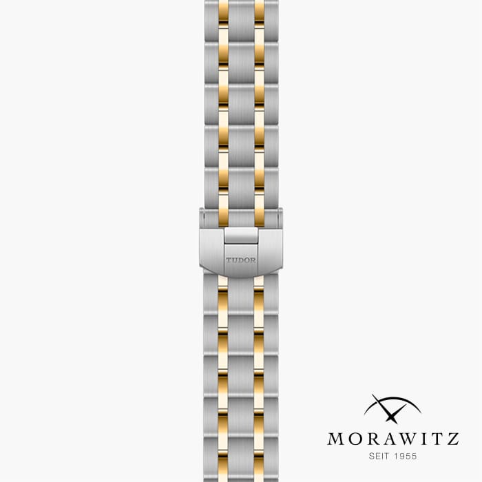 Bild eines Metallarmbands mit einem abwechselnden Muster aus silbernen und goldenen Gliedern. Das Armband trägt die Aufschrift „Tudor“ und ist vertikal angebracht. Das Logo „Morawitz, seit 1955“ mit gekreuzten Bögen über dem Namen erscheint in der unteren rechten Ecke.