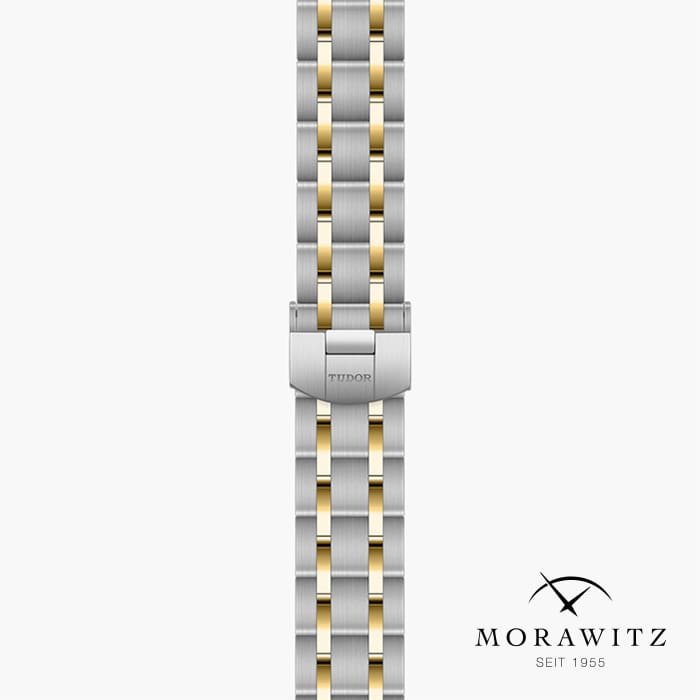 Bild, das eine Nahaufnahme eines Uhrenarmbands der Marke Tudor zeigt. Das Armband weist ein zweifarbiges Design mit silbernen und goldenen Gliedern auf. Unter dem Armband befindet sich das Morawitz-Logo, das den Text „Morawitz seit 1955“ und ein gekreuztes Schwert- und Nadelsymbol enthält.