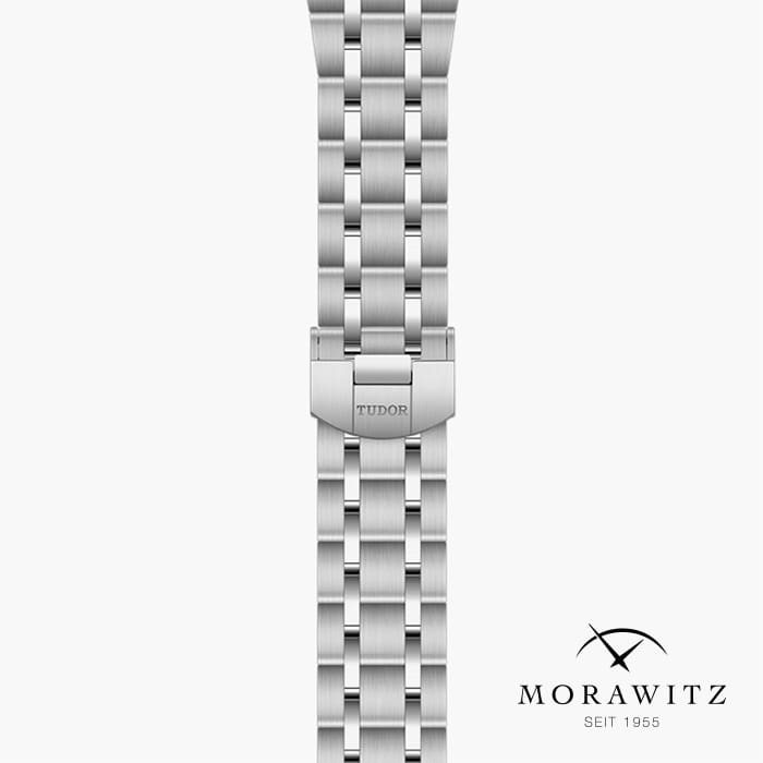 Eine Nahaufnahme eines silbernen Metalluhrarmbands mit einem Verschluss, in den der Markenname „Tudor“ eingraviert ist. In der unteren rechten Ecke sind das Logo und der Text „Morawitz seit 1955“ in Schwarz zu lesen. Der Hintergrund ist weiß.
