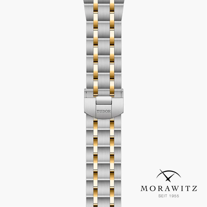 Ein silber-goldenes Tudor-Uhrenarmband mit Edelstahlverschluss und dem Markennamen. Der Hintergrund ist schlicht weiß und in der unteren rechten Ecke ist das Morawitz-Logo zusammen mit „Seit 1955“ zu sehen.