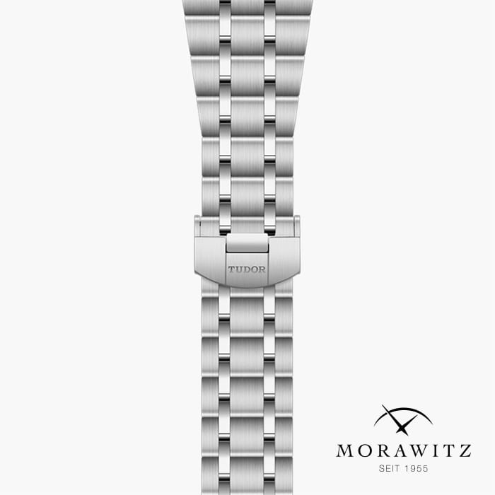 Ein Bild eines silbernen Metalluhrarmbands mit der Gravur „TUDOR“ auf dem Verschluss. Das Armband hat ein fünfgliedriges Design und sitzt auf einem weißen Hintergrund. Das Logo „MORAWITZ SEIT 1955“ mit zwei sich kreuzenden Linien ist in der unteren rechten Ecke sichtbar.