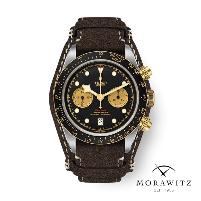 Eine luxuriöse Tudor-Chronographenarmbanduhr mit schwarzem Zifferblatt, zwei goldenen Hilfszifferblättern, goldenen Zeigern und schwarzer Lünette. Die Uhr verfügt über eine Datumsanzeige auf der 6-Uhr-Position und ein dunkelbraunes Lederarmband mit kontrastierenden weißen Nähten. Das Morawitz-Logo ist darunter sichtbar.