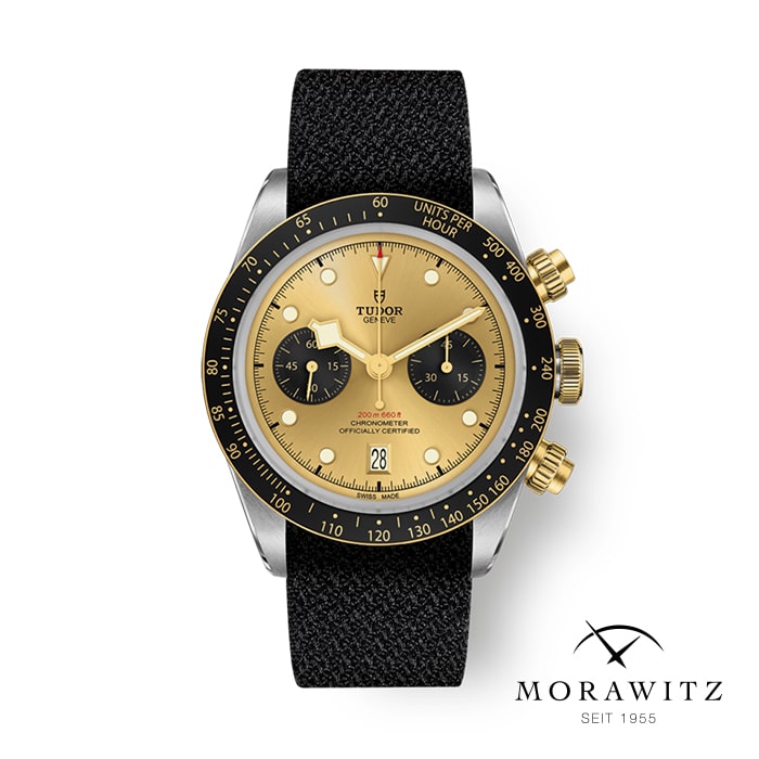 Eine luxuriöse Tudor-Armbanduhr mit schwarzem Stoffarmband und goldener Lünette. Die Uhr verfügt über einen Chronographen mit zwei Hilfszifferblättern, eine Datumsanzeige bei 6 Uhr und ist von einer Tachymeterskala umgeben. Unten sind das Morawitz-Logo und „SEIT 1955“ abgebildet.