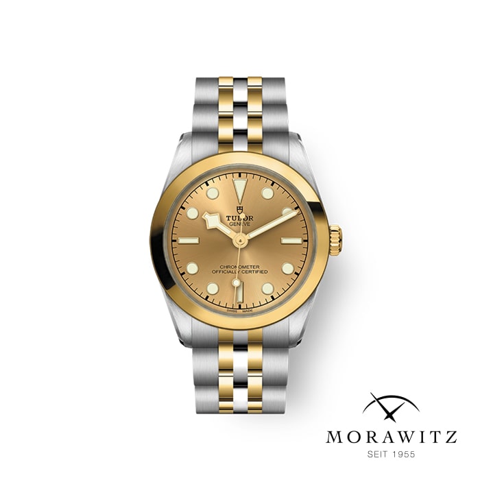 Eine Armbanduhr aus Edelstahl und Gold mit rundem Zifferblatt und Tudor-Logo. Die goldene Lünette umgibt ein passendes goldenes Zifferblatt mit einfachen Markierungen und Zeigern. Das Armband hat abwechselnd goldene und silberne Glieder. Darunter ist das Logo „MORAWITZ SEIT 1955“ abgebildet.