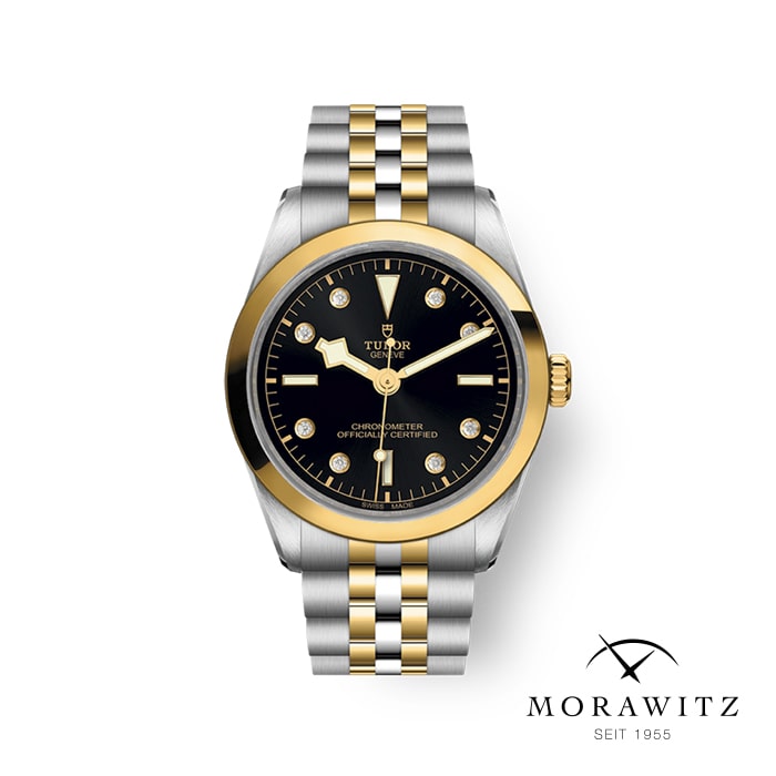 Eine Luxusarmbanduhr mit einem Armband aus Edelstahl und Gold, einem schwarzen Zifferblatt mit goldenen Akzenten und Diamant-Stundenmarkierungen. Die Uhr trägt die Marke „Tudor“ und hat in der unteren rechten Ecke das „Morawitz“-Logo mit „SEIT 1955“ darunter.