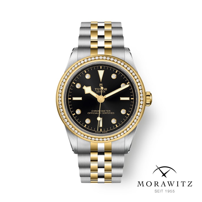 Eine Tudor-Armbanduhr aus Gold und Silber mit schwarzem Zifferblatt, goldfarbenen Zeigern und Diamant-Stundenmarkierungen wird ausgestellt. Die Lünette ist mit Diamanten verziert. Der Markenname der Uhr „Tudor“ ist auf dem Zifferblatt zu sehen und das Logo „Morawitz Seit 1955“ befindet sich in der unteren rechten Ecke.