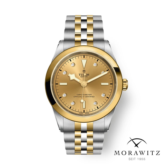 Eine Tudor-Armbanduhr mit goldenem Zifferblatt und Diamant-Stundenmarkierungen sowie einem zweifarbigen Metallarmband mit goldenen und silbernen Gliedern. Die Uhr ist über dem Morawitz-Logo angebracht, das den Text „MORAWITZ SEIT 1955“ und ein stilisiertes geschwungenes Liniendesign enthält.