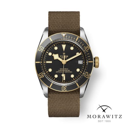 Eine stilvolle Armbanduhr mit braunem Lederarmband und schwarzem Zifferblatt. Sie hat eine goldfarbene Lünette mit Minutenmarkierungen, leuchtenden Zeigern und Indizes. Die Uhr verfügt über ein Datumsfenster auf der 3-Uhr-Position. Unten rechts sind das Wort „MORAWITZ“ und das Logo vorhanden.