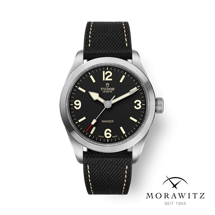 Eine schwarze Tudor Ranger-Uhr mit rundem Edelstahlgehäuse und schwarzem Stoffarmband. Sie verfügt über arabische Ziffern bei 3, 6, 9 und 12 sowie leuchtende Zeiger und Stundenmarkierungen. Das Markenlogo und „Tudor“, „Geneve“ und „Ranger“ sind auf dem Zifferblatt zu sehen. Das Morawitz-Logo befindet sich in der unteren rechten Ecke.