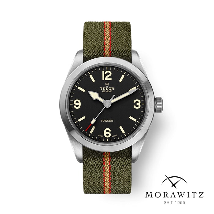 Eine Tudor Ranger-Armbanduhr mit schwarzem Zifferblatt, leuchtenden Zeigern und Markierungen und einem grünen Stoffarmband mit einem roten Streifen in der Mitte. Vor einem weißen Hintergrund mit dem Logo „Morawitz Seit 1955“ in der unteren rechten Ecke verkörpert dieses zeitlose Stück robuste Eleganz.