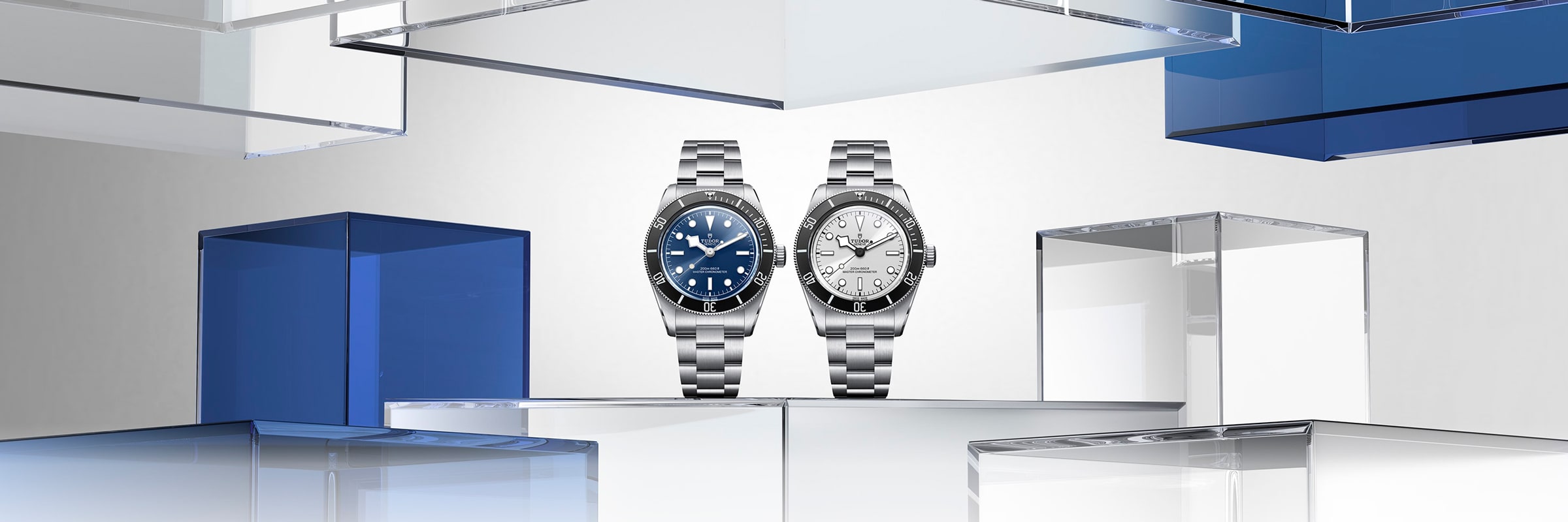 Zwei silberne Armbanduhren mit Metallbändern stehen aufrecht vor einem minimalistischen Hintergrund mit transparenten und blauen glasähnlichen rechteckigen Formen. Die linke Uhr hat ein blaues Zifferblatt, die rechte Uhr ein weißes Zifferblatt.