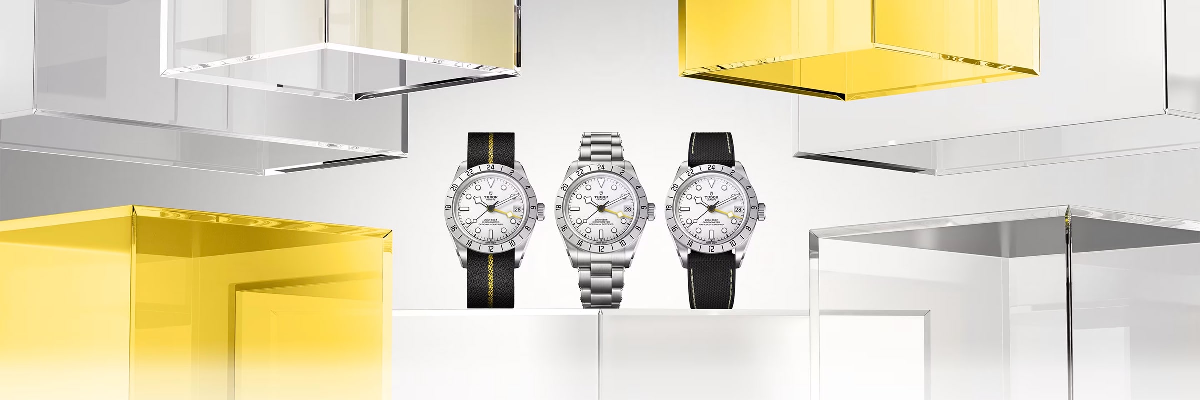 Drei Luxusarmbanduhren mit weißen Zifferblättern sind aufrecht aufgestellt; eine hat ein schwarzes Armband, eine ein silbernes Metallband und eine ein zweifarbiges Armband. Sie sind von transparenten und gelb gefärbten geometrischen Blöcken umgeben.