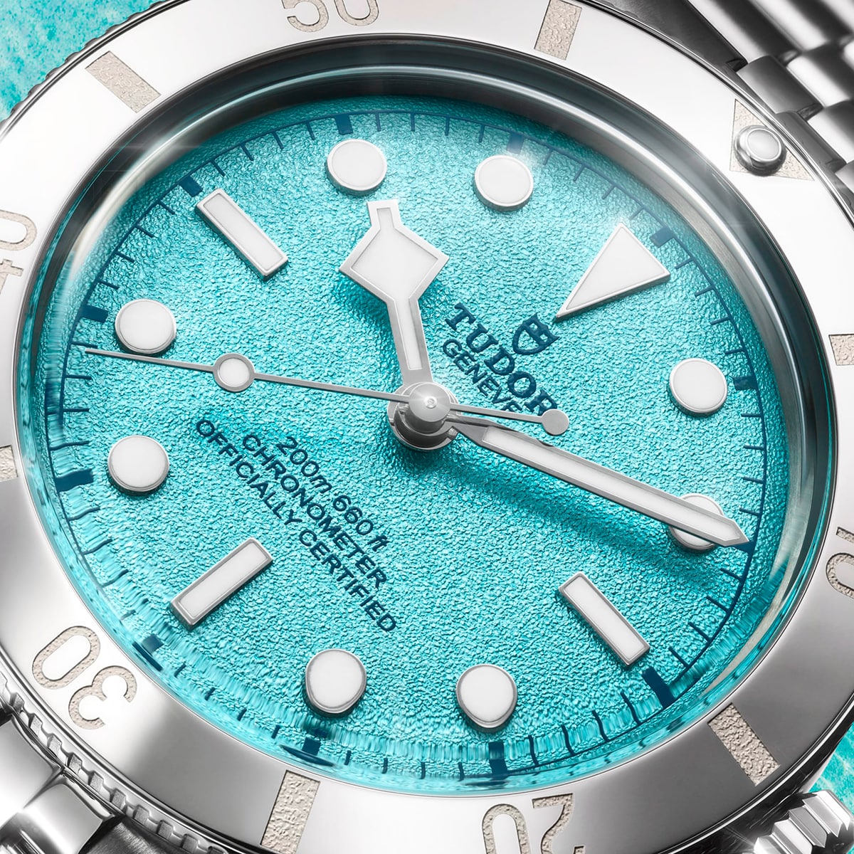 Nahaufnahme einer TUDOR Black Bay 54 "Lagoon Blue" Armbanduhr mit strukturiertem türkisfarbenem Zifferblatt, silbernen Indexen, Datumsfenster bei 3 Uhr und dem Text "Officially Certified". Die Lünette und das Armband aus Edelstahl sind ebenfalls sichtbar.