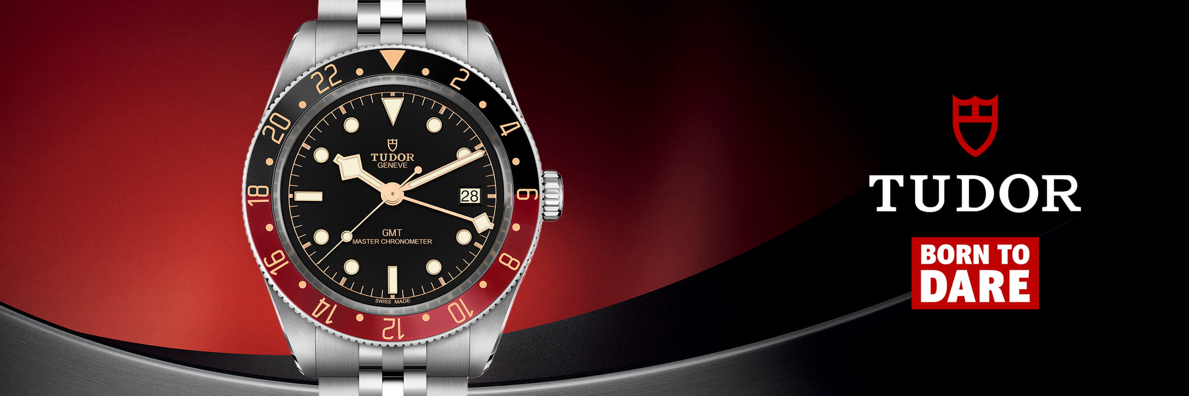 Eine Tudor GMT-Armbanduhr mit schwarzem Zifferblatt, rot-blauer Lünette und silbernem Armband wird auf einem rot-schwarzen Hintergrund neben dem markanten Tudor-Logo und dem Slogan Born to Dare" in auffälliger weiß-roter Schrift präsentiert.